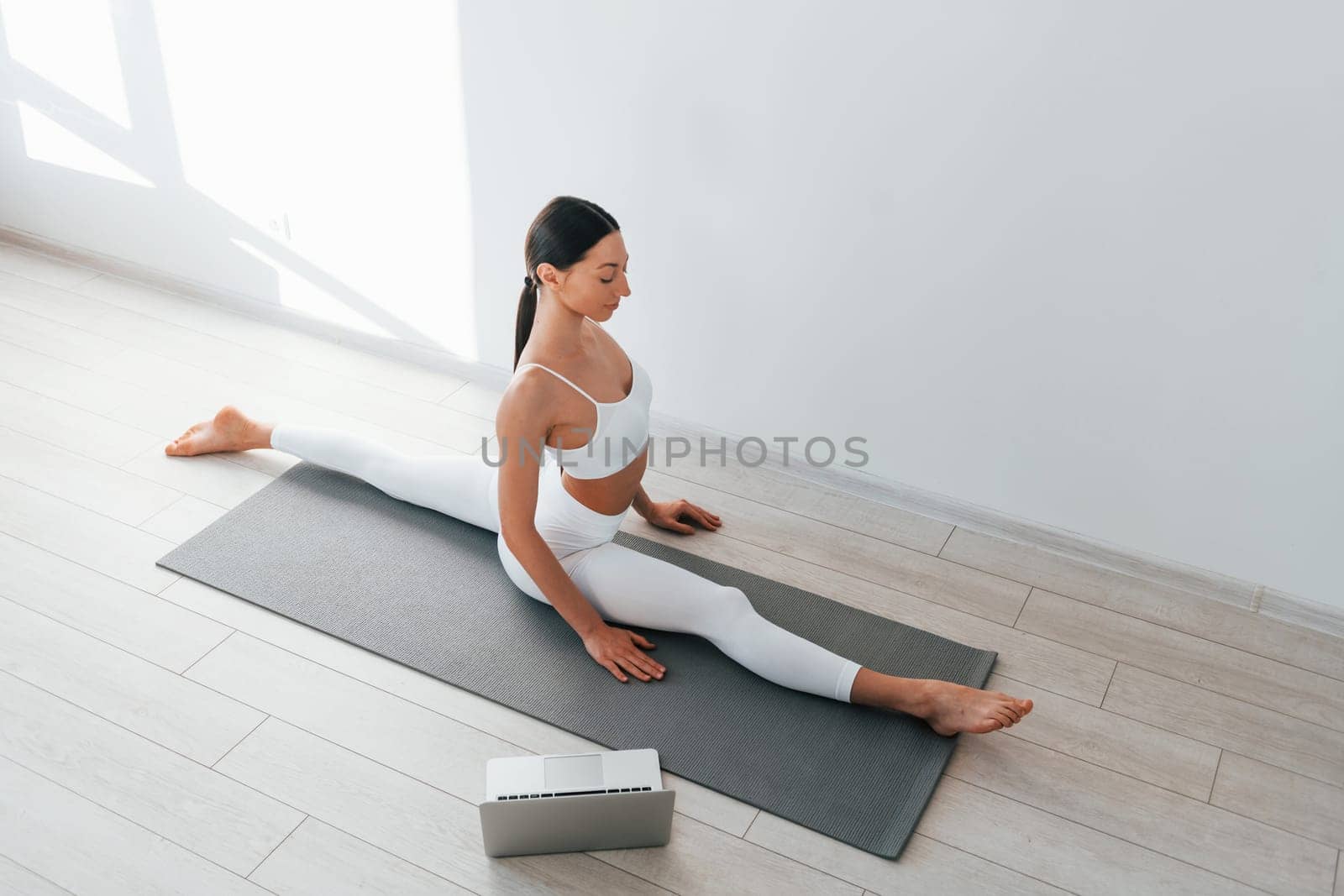 On yoga mat. Young caucasian woman with slim body shape is indoors at daytime.