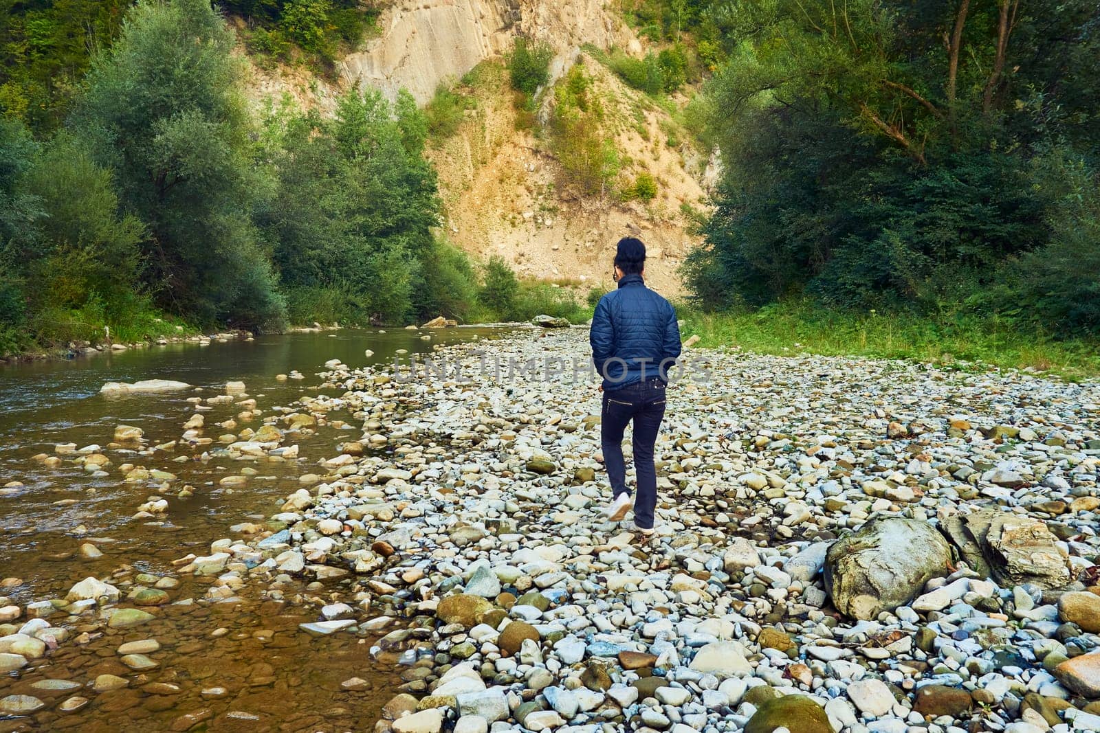 Young woman walking along the wild rocky shallow bank of a mountain river by jovani68