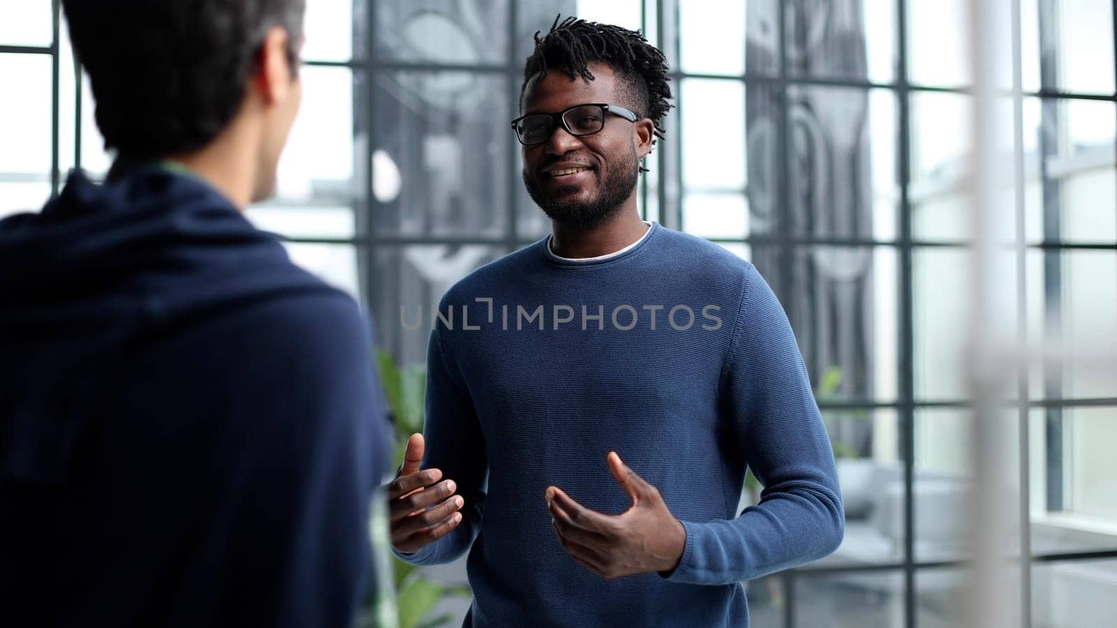 Diverse male colleagues in modern office corridor, young african american and caucasian business people discussing common project work, meeting in company work