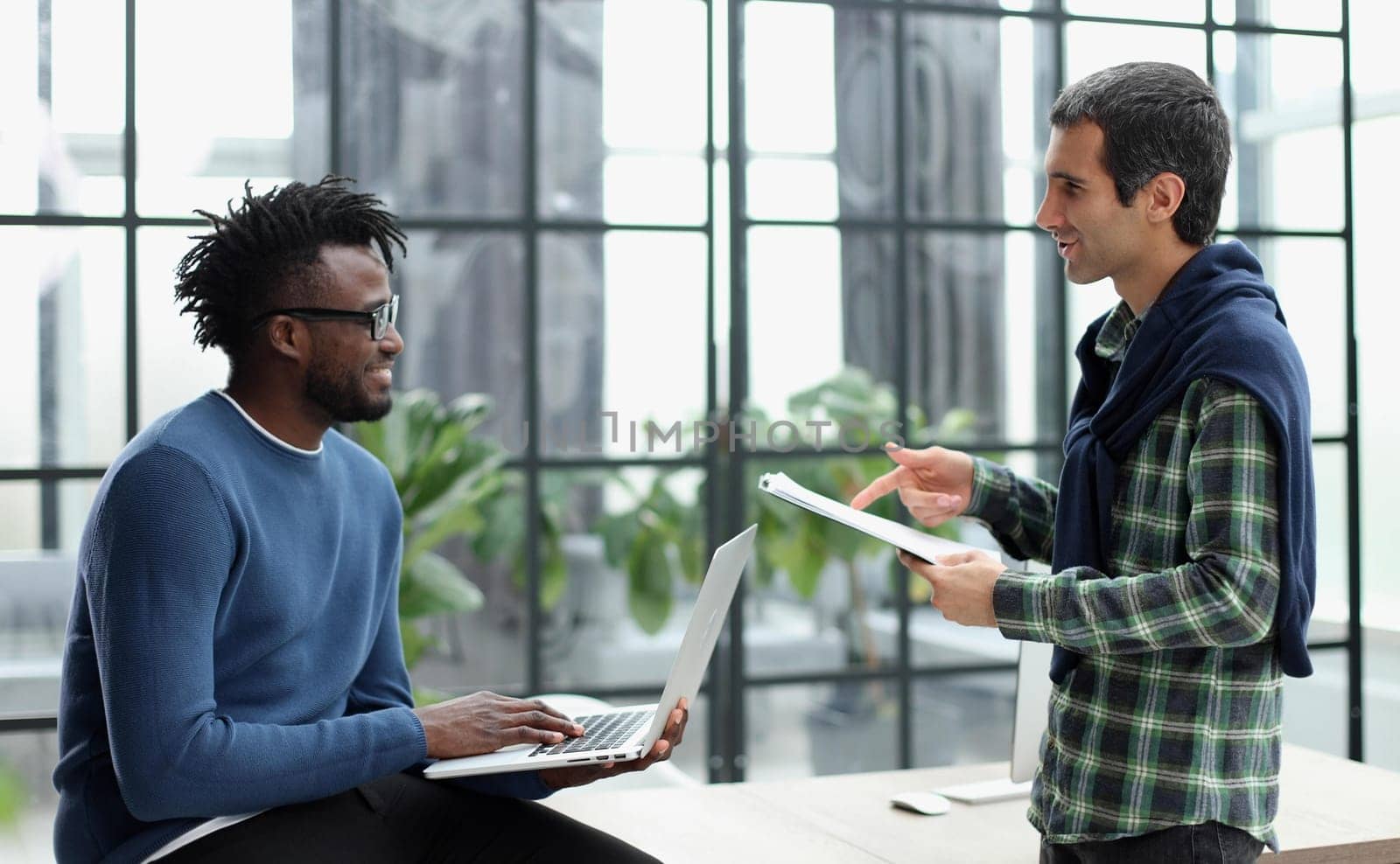 Young businessman holding laptop while discussing new project with african american colleague