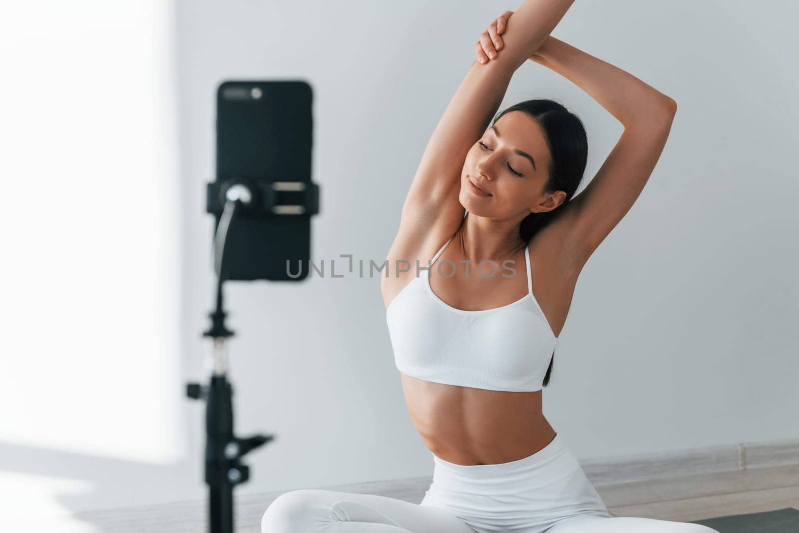 Phone on tripod. Young caucasian woman with slim body shape is indoors at daytime.