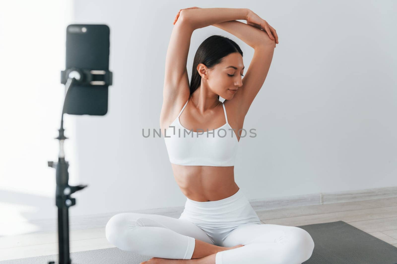 Phone on tripod. Young caucasian woman with slim body shape is indoors at daytime.