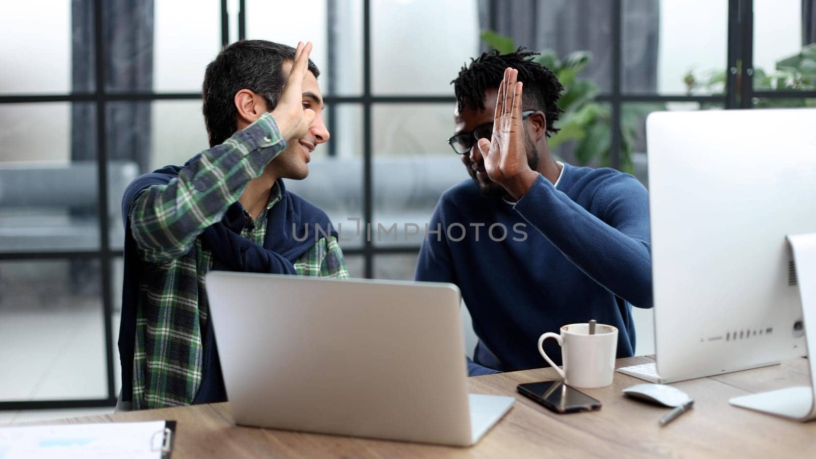Happy multicultural programmers giving high five while working in office togethe