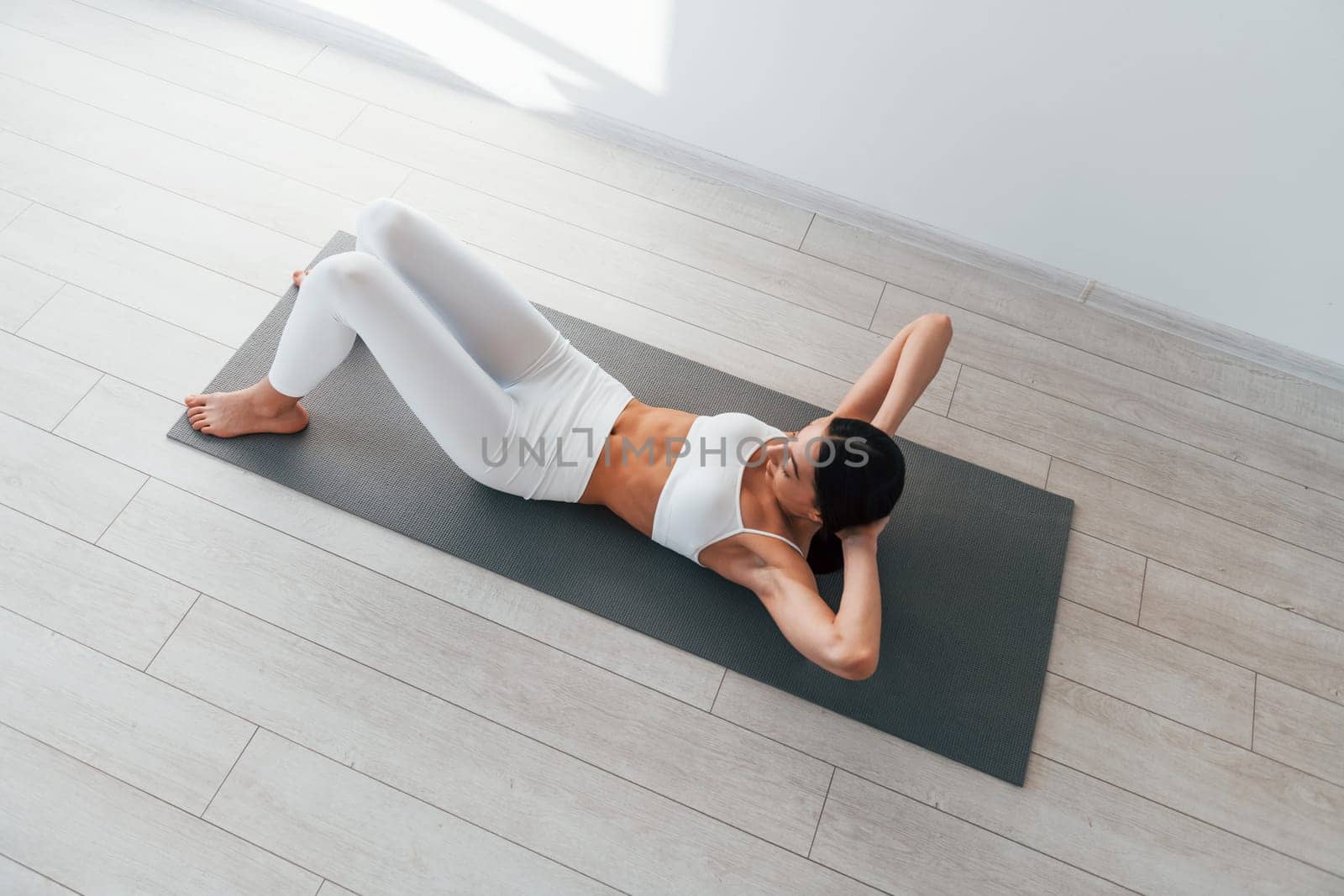 Doing exercises. Young caucasian woman with slim body shape is indoors at daytime by Standret