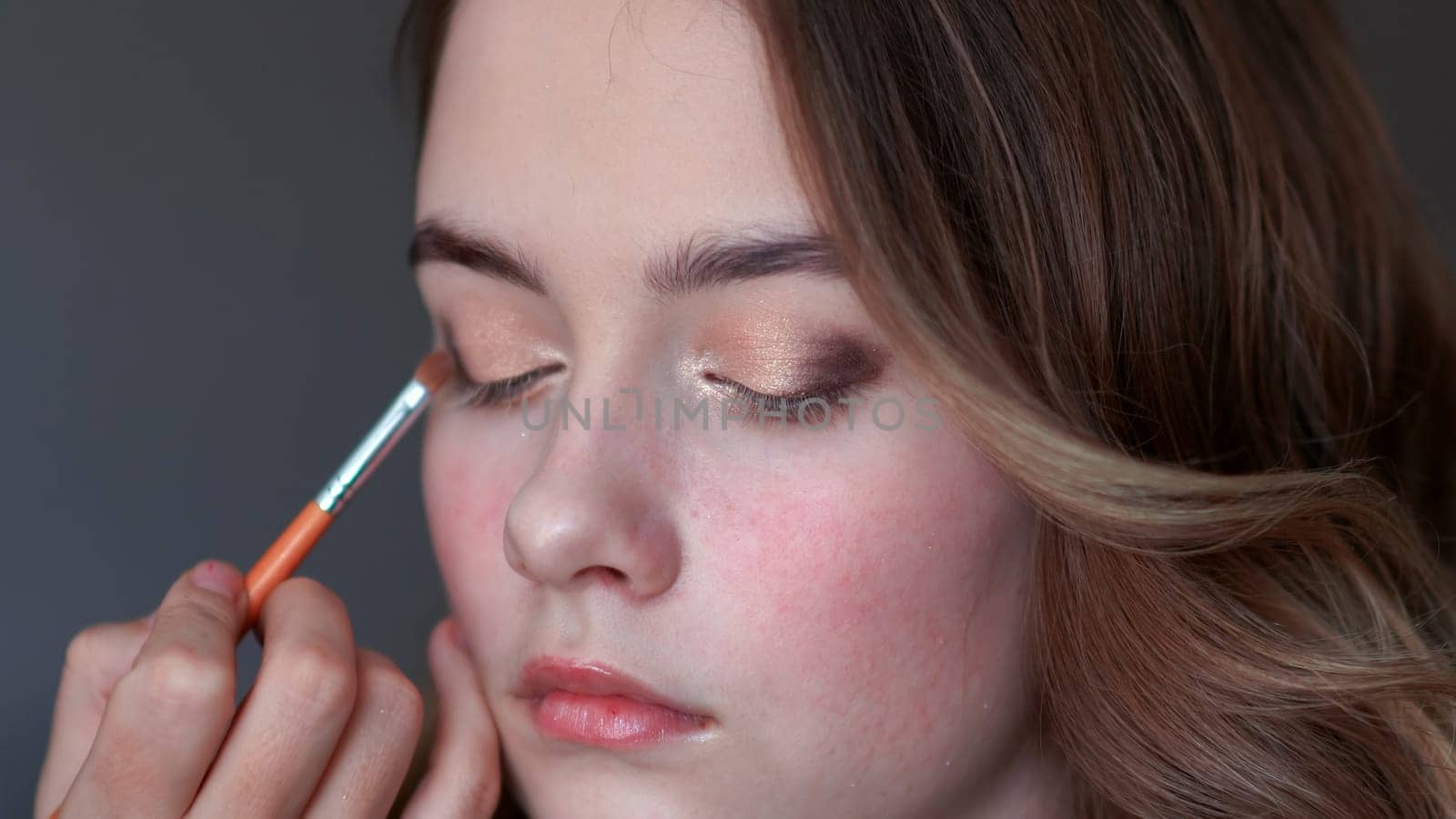 Girl makeup artist paints the eyelids of a girl model.