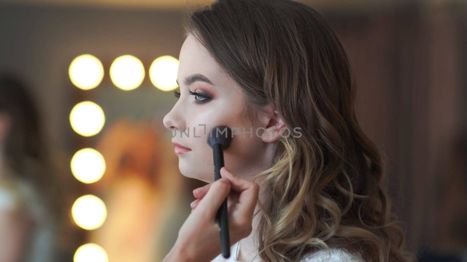 Makeup artist applies powder on the face of a 16 year old girl