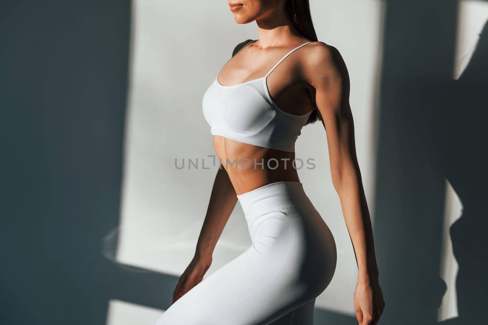 In white sportive clothes. Young caucasian woman with slim body shape is indoors at daytime.