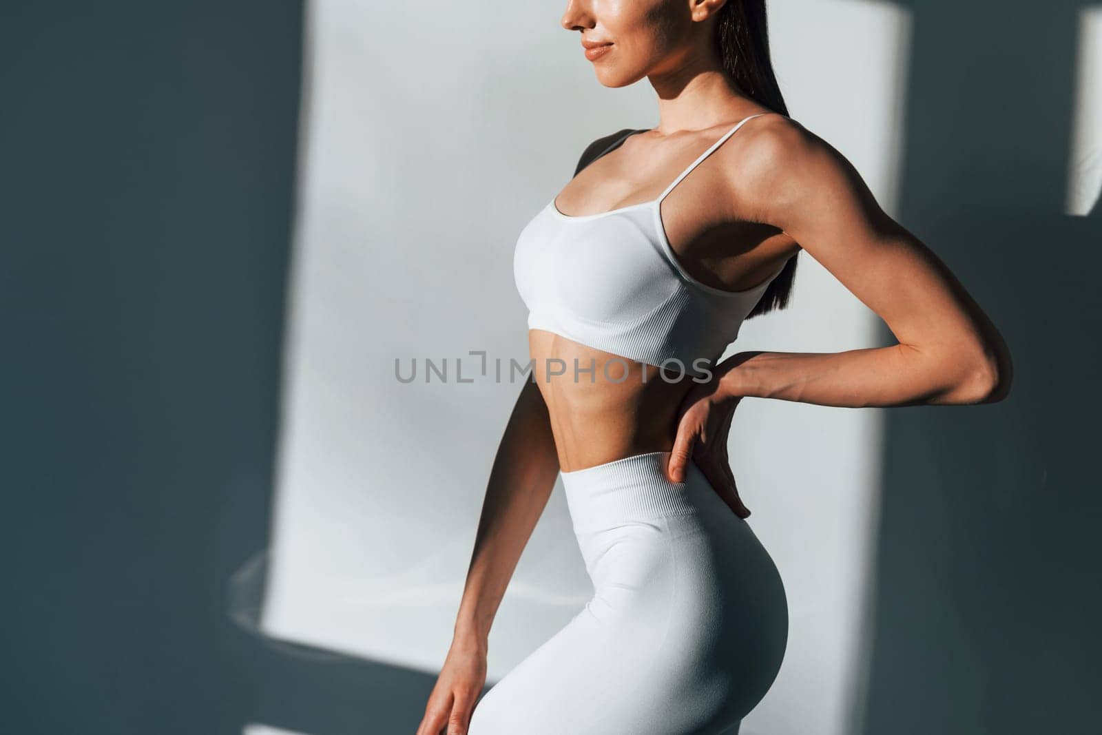 In white sportive clothes. Young caucasian woman with slim body shape is indoors at daytime.