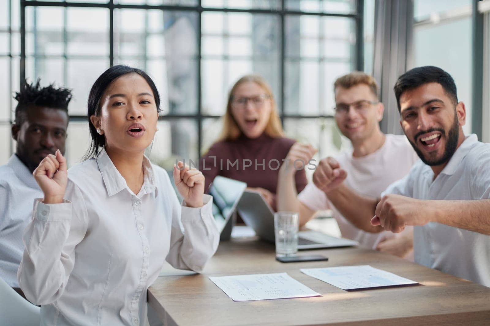 group of different business people celebrating victory while sitting at table in modern office by Prosto