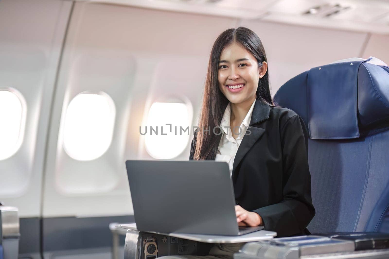 Female passenger sitting on plane while working on laptop computer with simulated space using on board wireless connection by wichayada