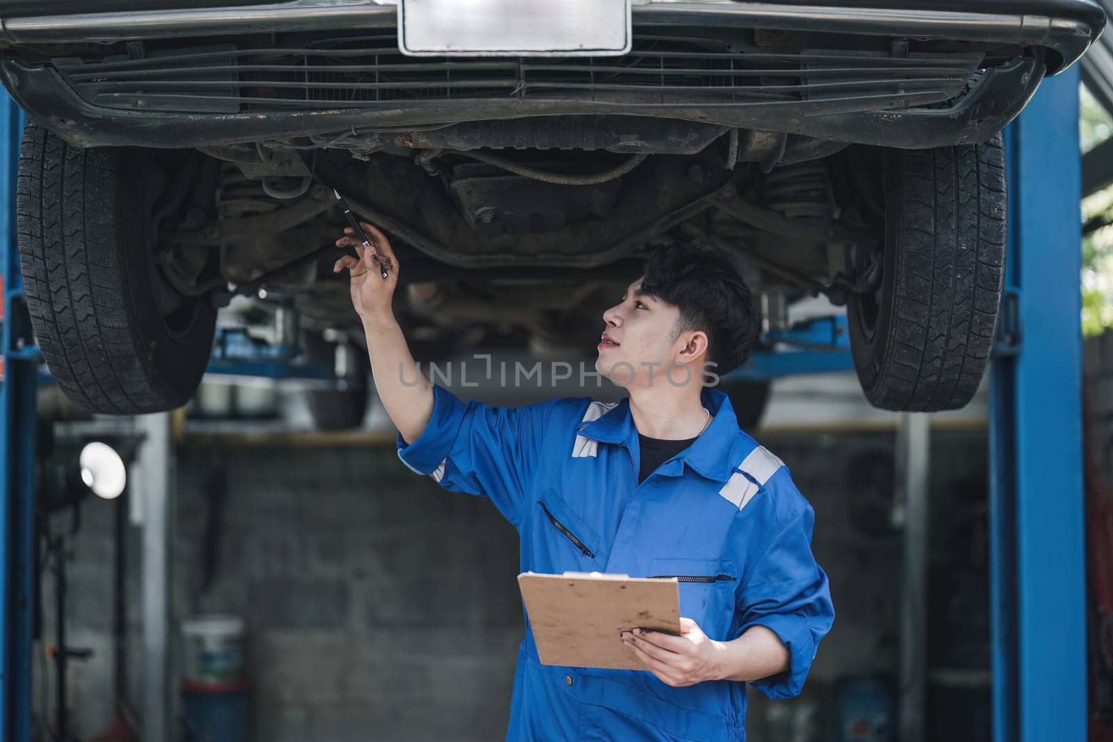 Vehicle service maintenance asian man checking under car condition in garage. Automotive mechanic maintenance checklist document. Car repair service concept..
