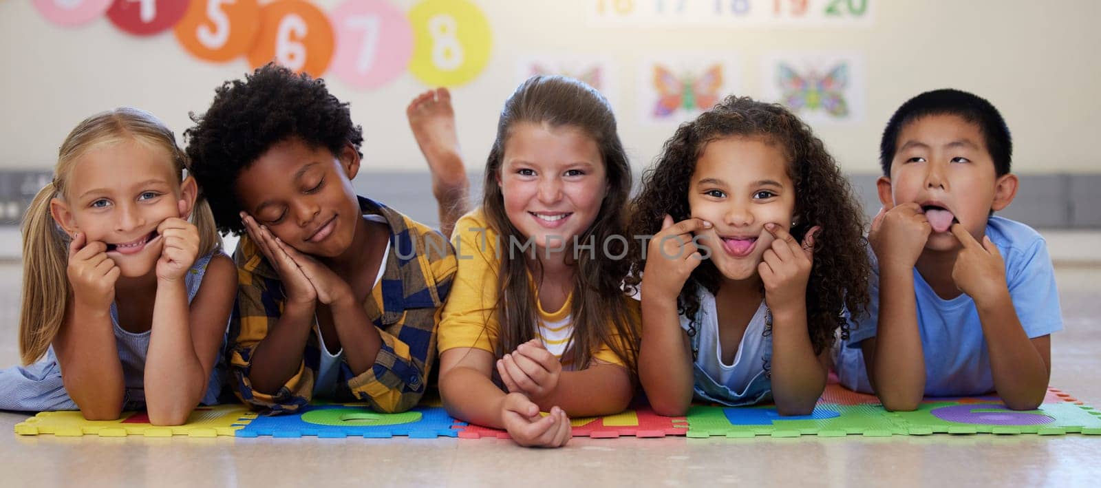 Kids, floor and group portrait with funny face in school classroom, solidarity or diversity in childhood. Girl, boy and children in class, academy and happy multicultural friends, together or playful by YuriArcurs