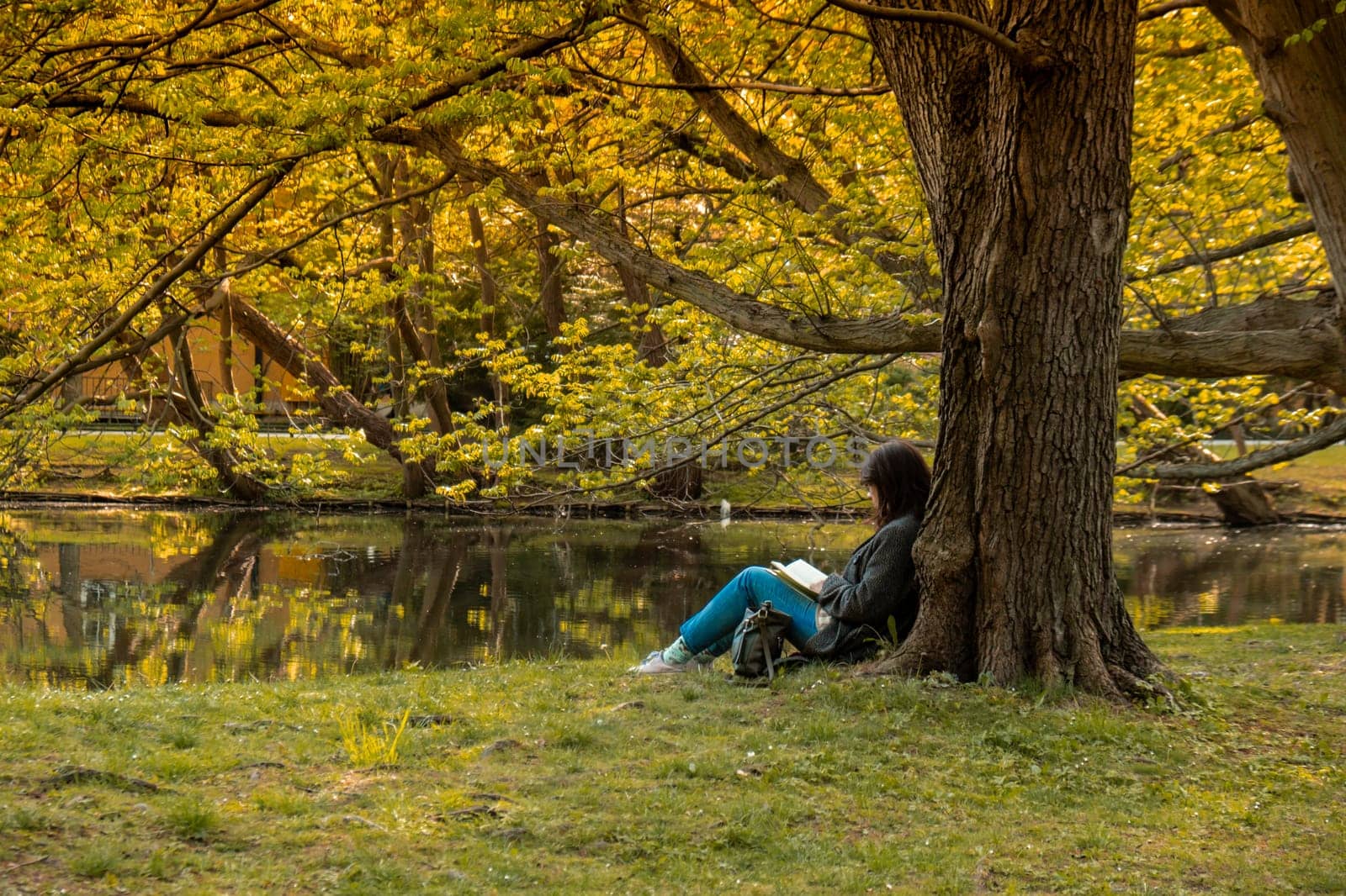 Attractive young woman reading book while sitting on grass in green public park. Springtime outdoors. Greenery unity with nature. Spend free time on open air. Education concept
