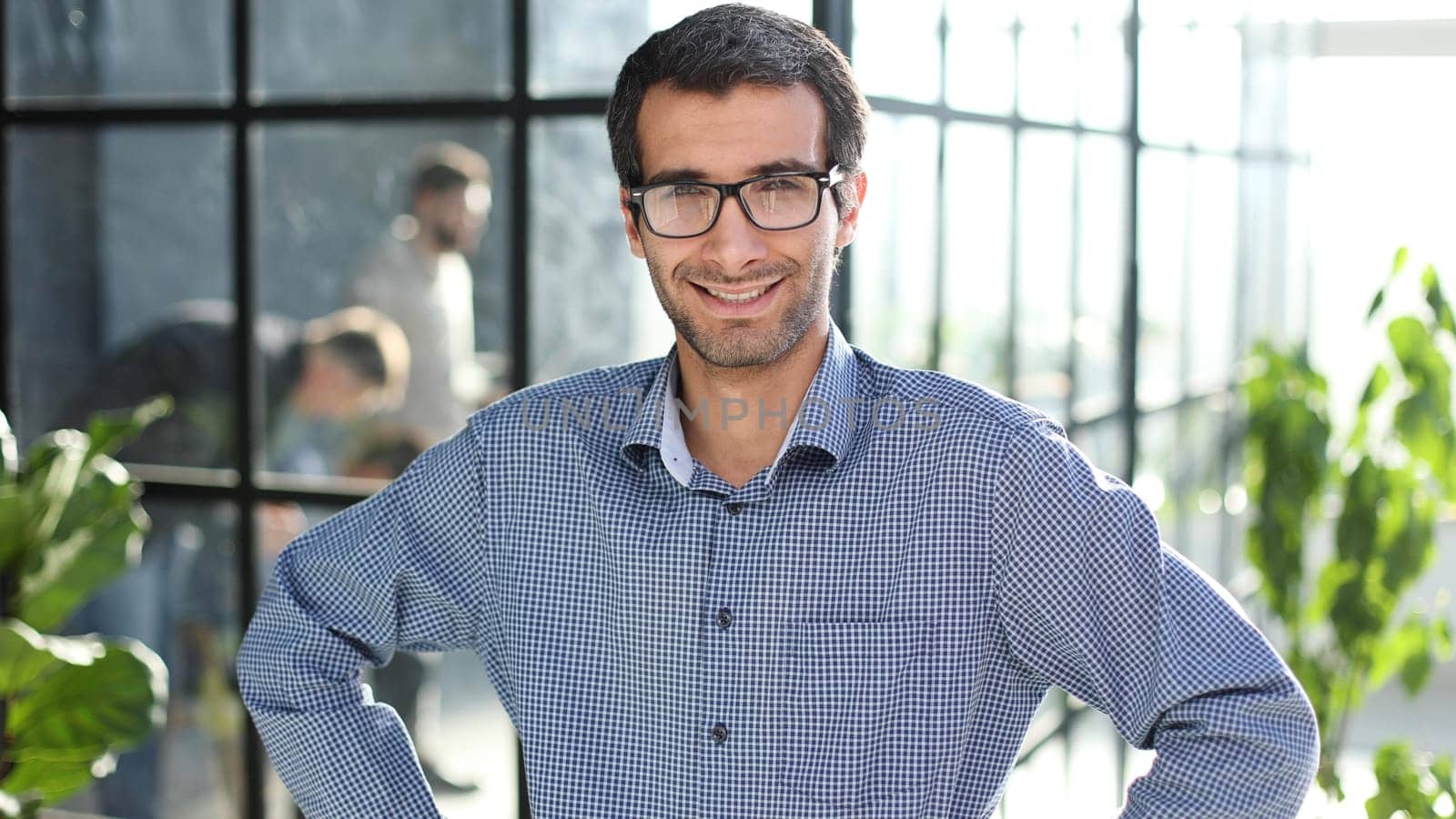 Young businessman in casual clothes stands with his hands on his waist in a modern office