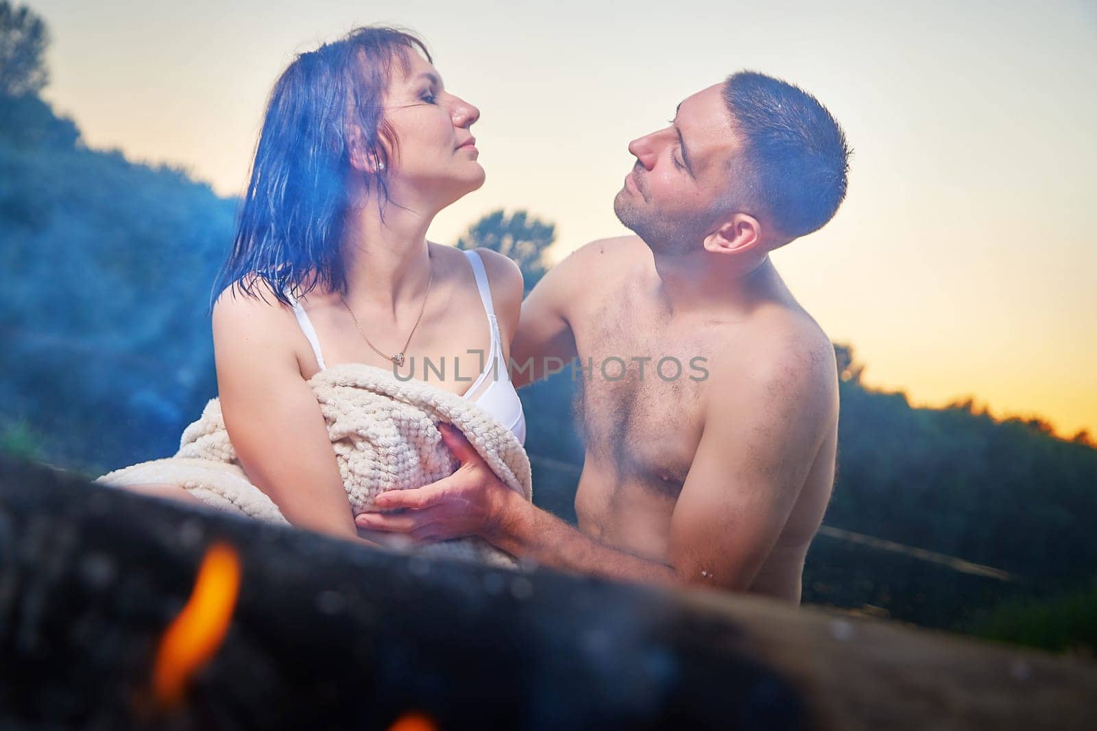 Happy Couple relaxin, having fun and hugs with fire in camping on nature near water of river or lake in summer sunny evening in sunset. Family or lovers have date and rest outdoors. Concept of love by keleny