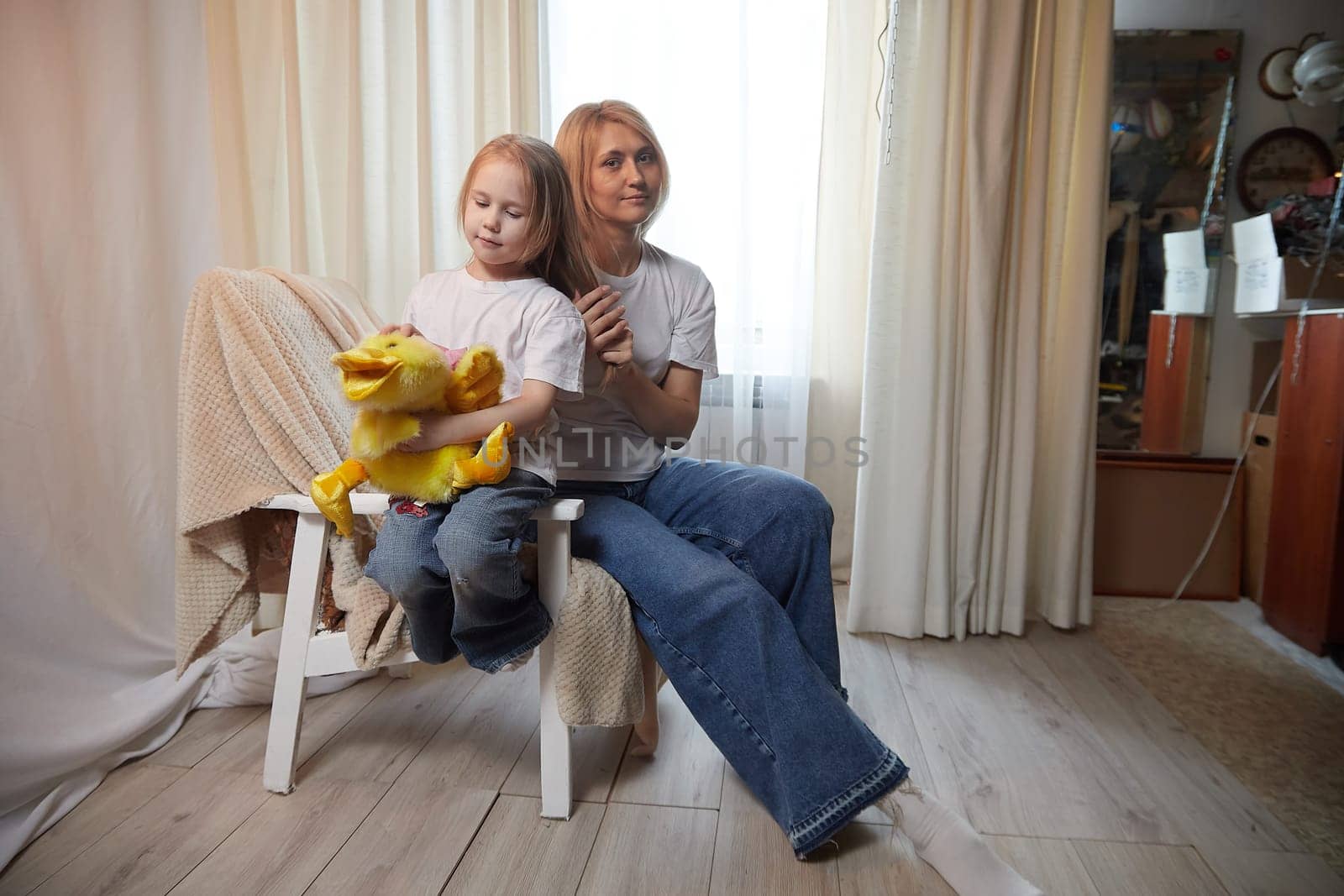 Happy loving family with mother and daughter in living room. Woman mom and small child girl playing and having convercation inside of the home by keleny