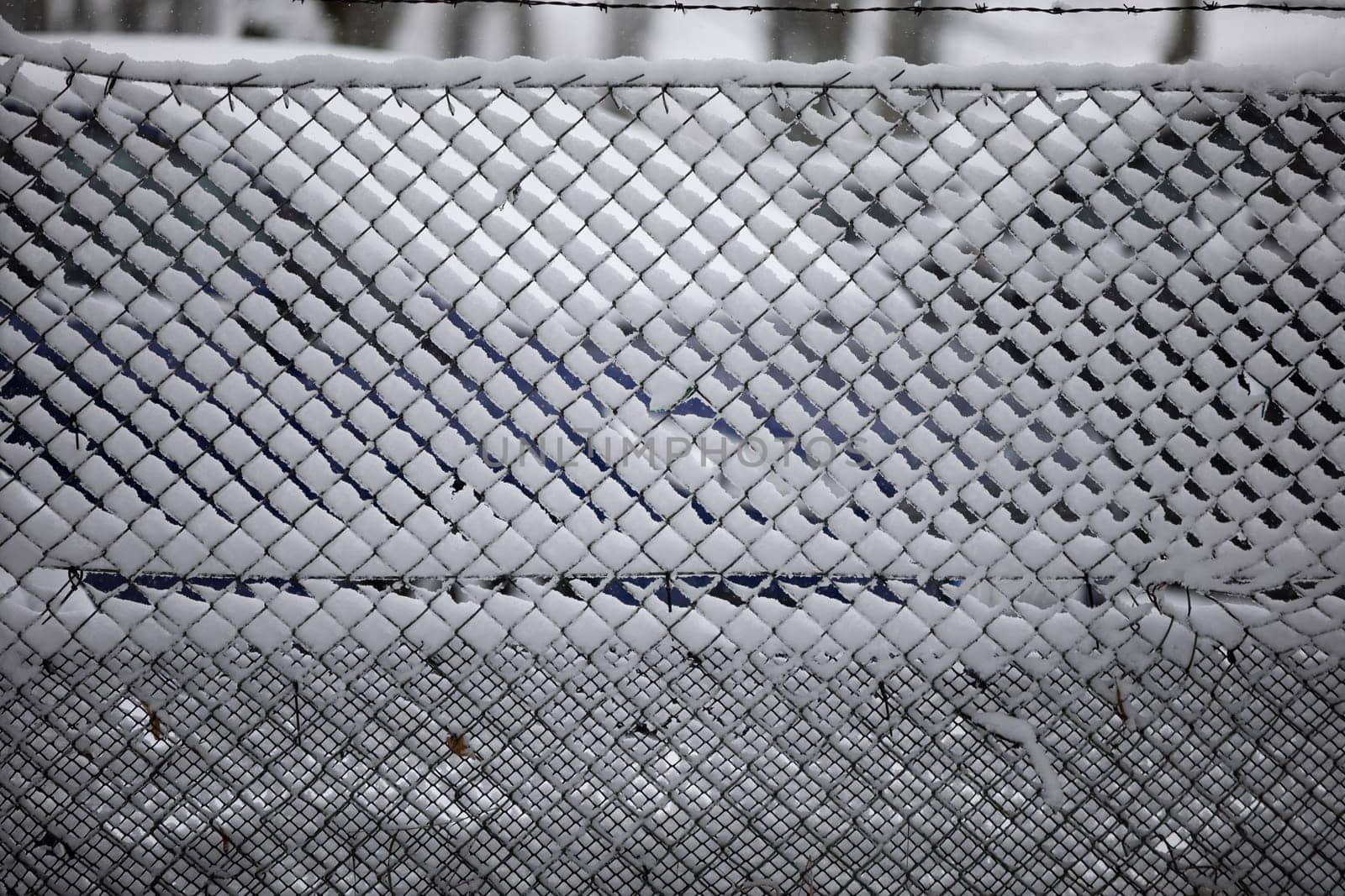 Snow has settled on a wire fence. Close-up of a frozen fence covered with snow. The spaces between the wire are filled with snow and ice.