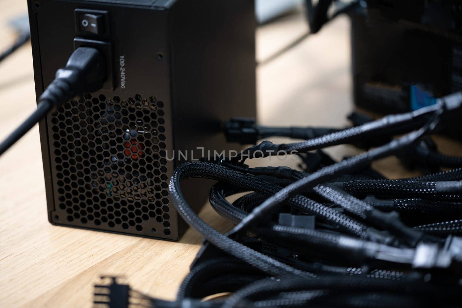 Black modular power cables for a computer lying on a brown wooden top. Close-up of black computer cables. Blurred foreground. A focused view of the cables in the background.