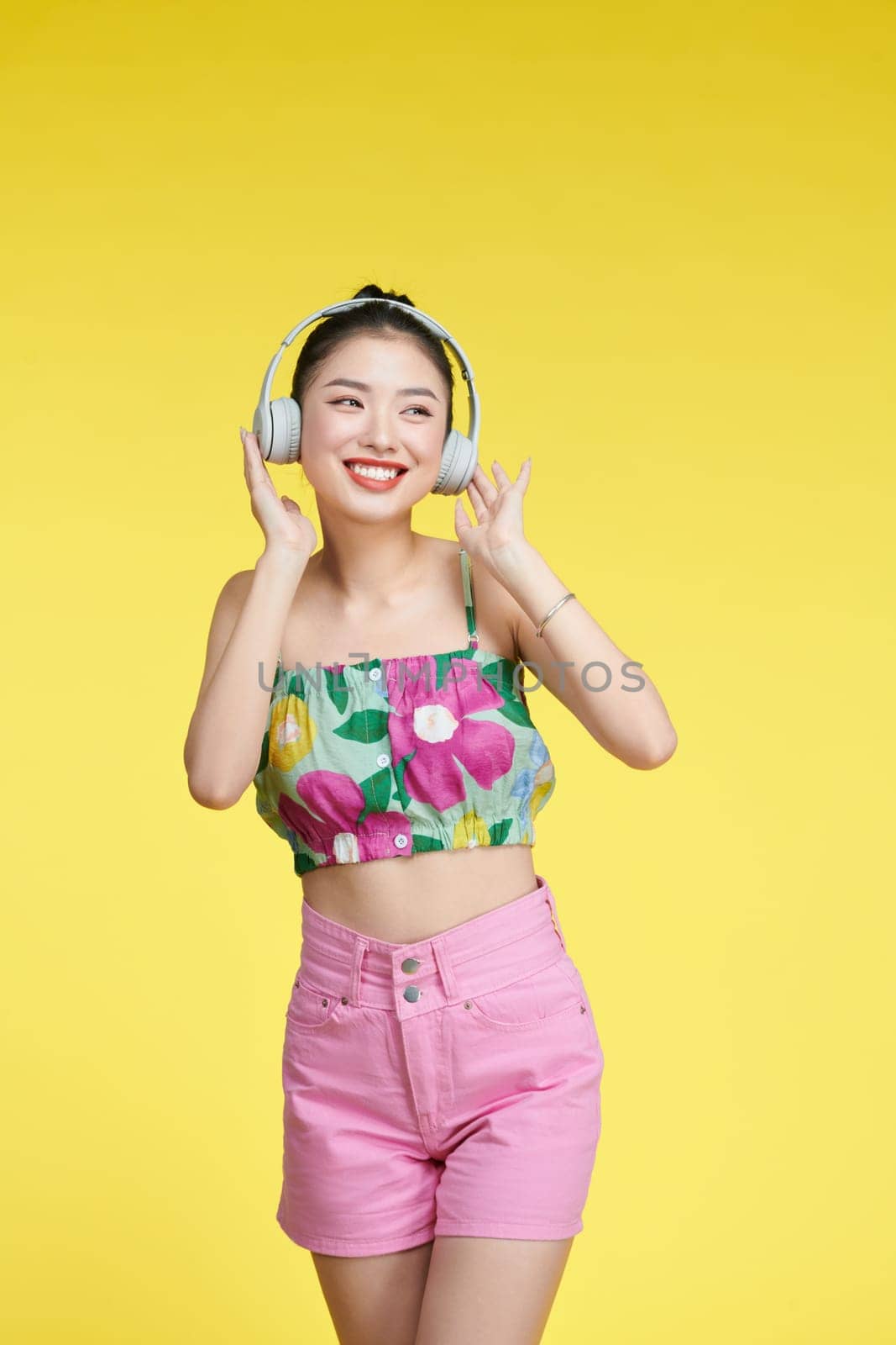 Cheerful young woman listen to music putting her hands on headphones isolated on yellow background