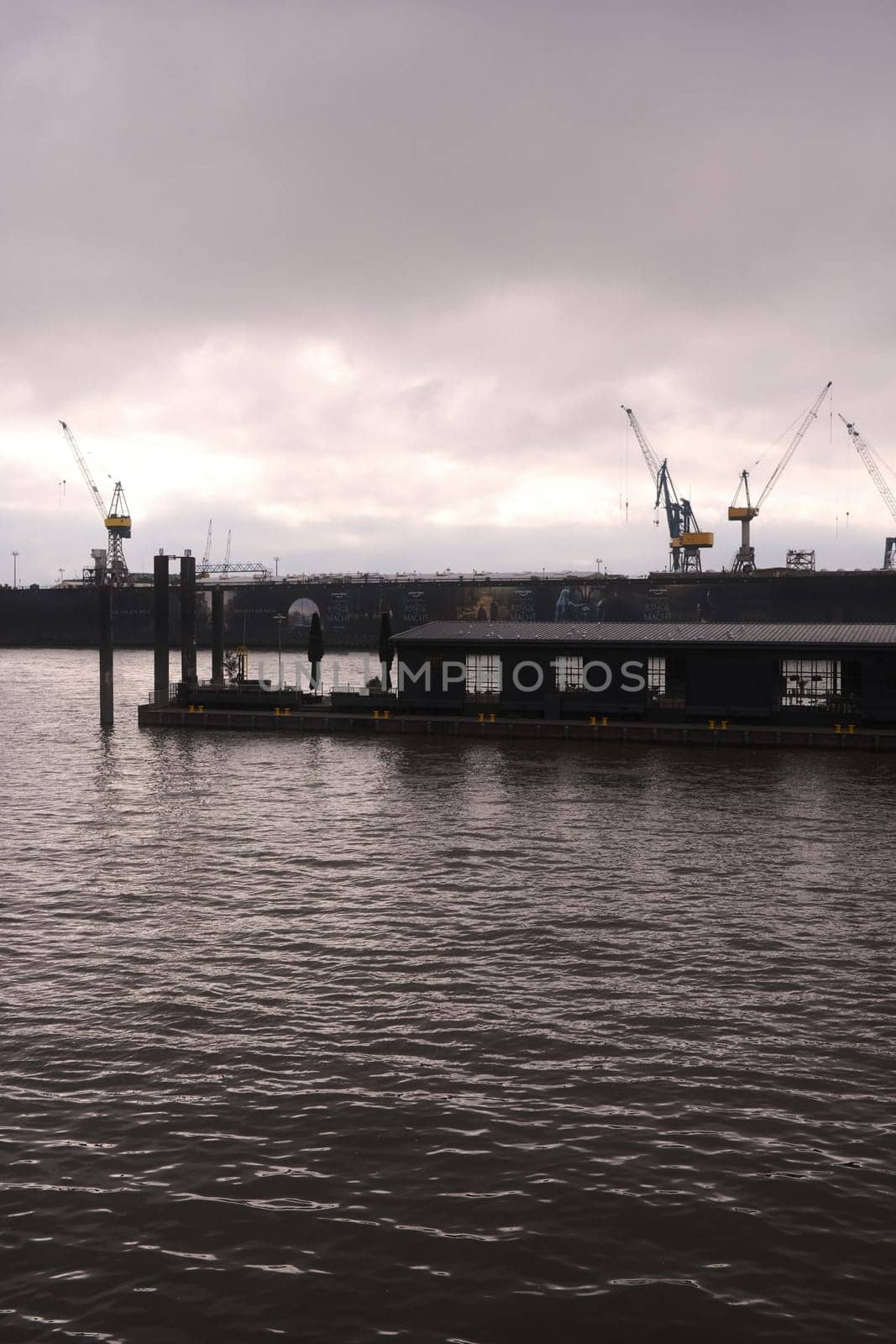 Vertical monochrome of a floating cafe on the water before the cranes in the port of Hamburg