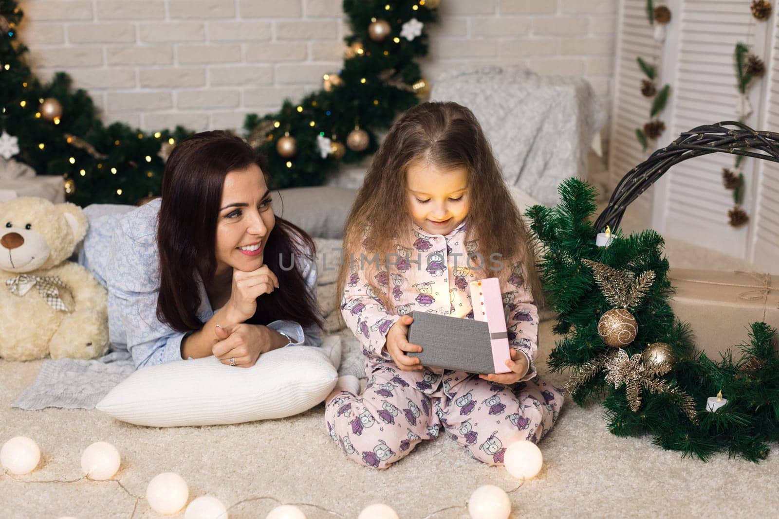 Pretty smiling child girl with mother opening magical box with Christmas gift at home