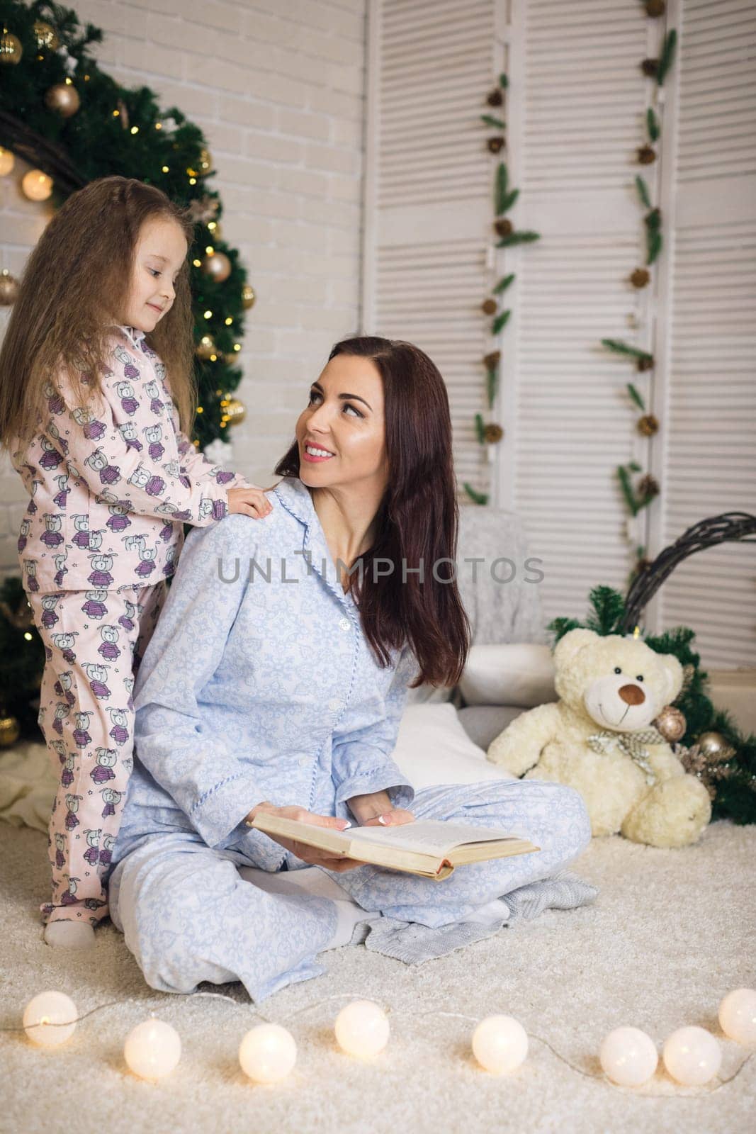 mother reading book to her little cute daughter near Christmas tree at home