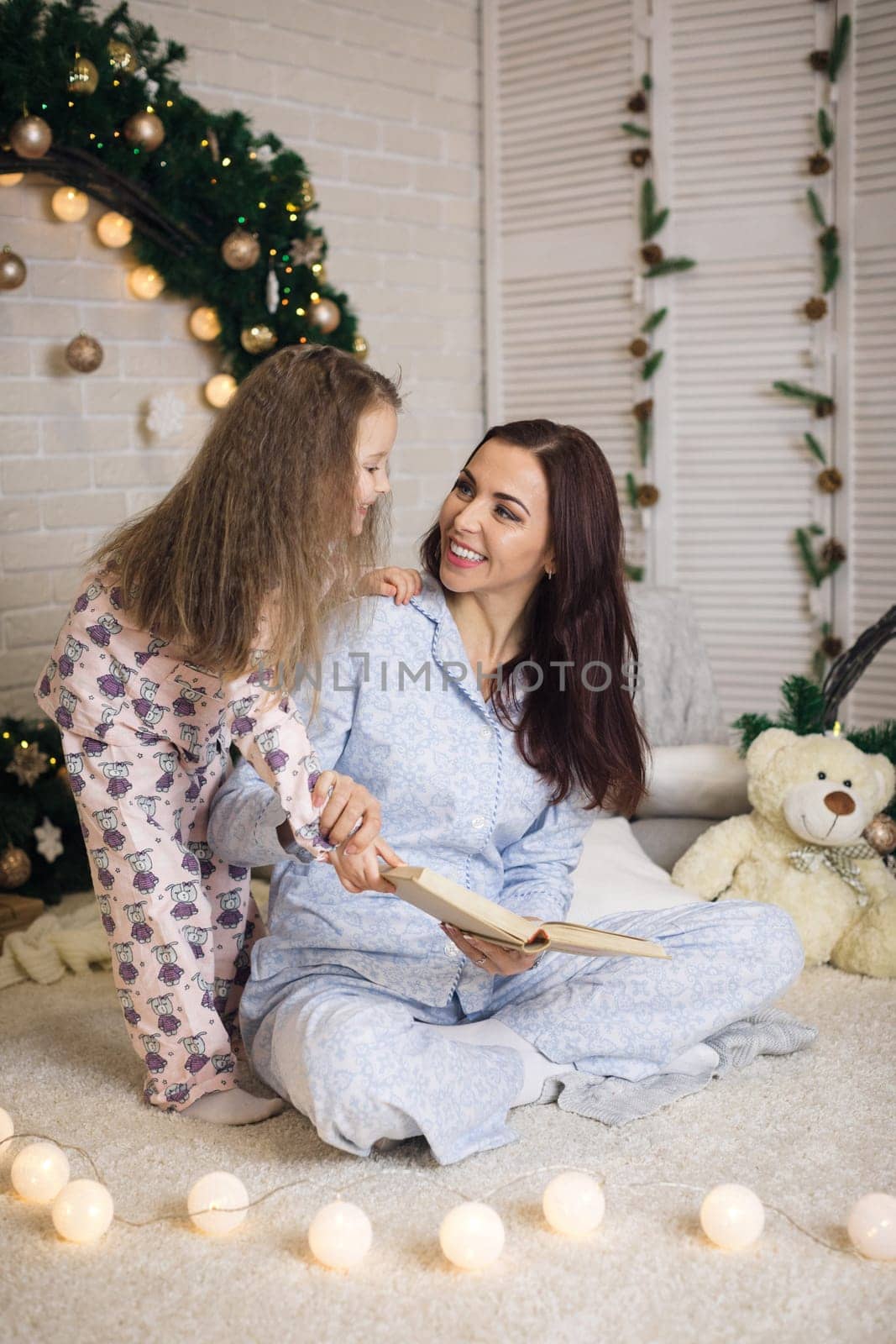 mother reading book to her little cute daughter near Christmas tree at home