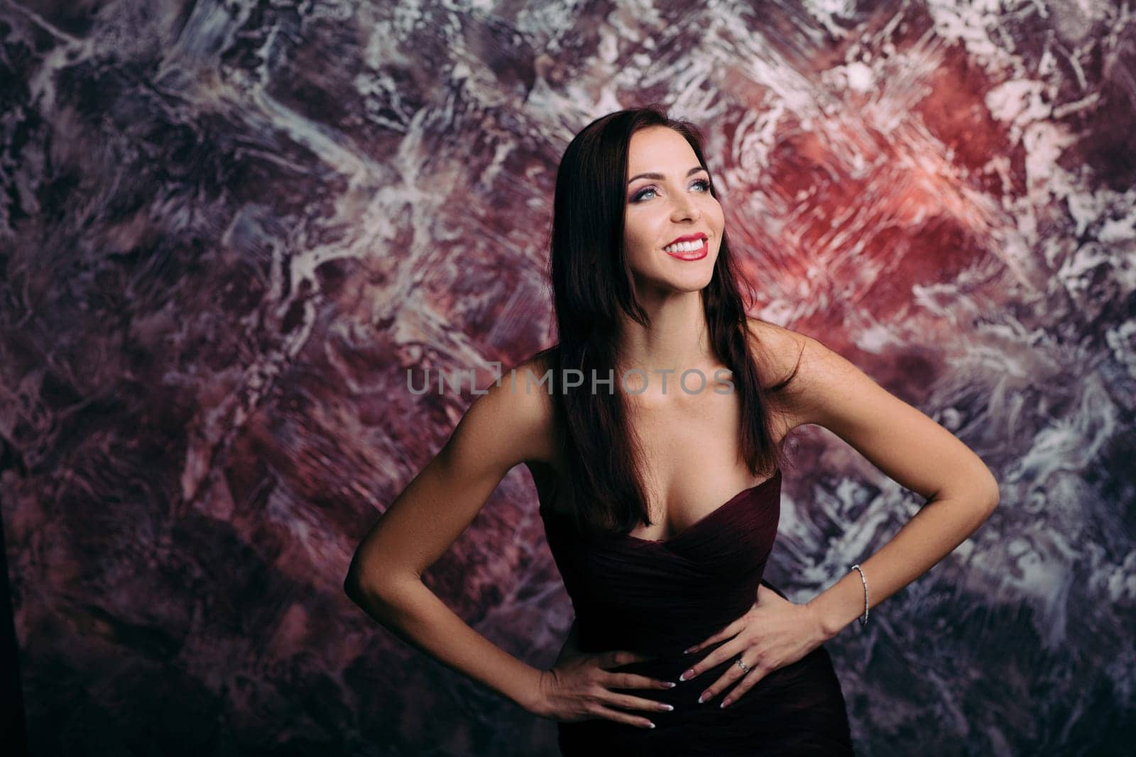 Portrait of magnificent sexy woman in evening dress posing over dark red background