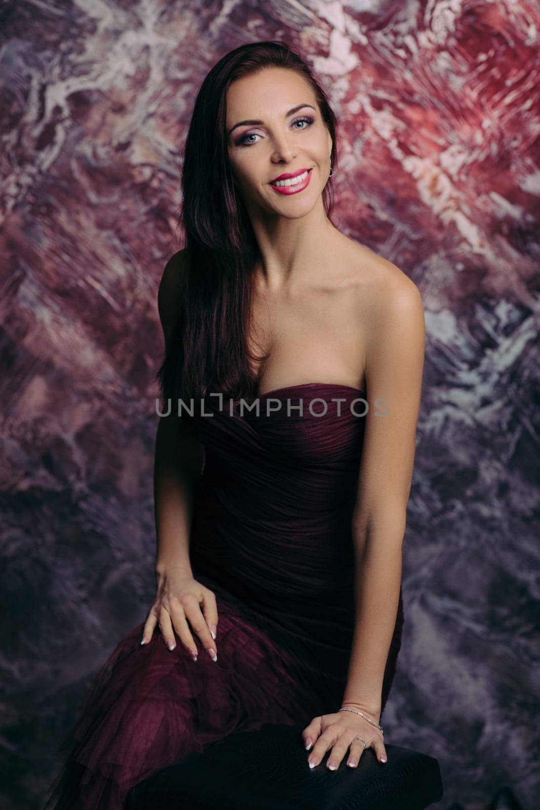 Portrait of magnificent sexy woman in evening dress posing over dark red background