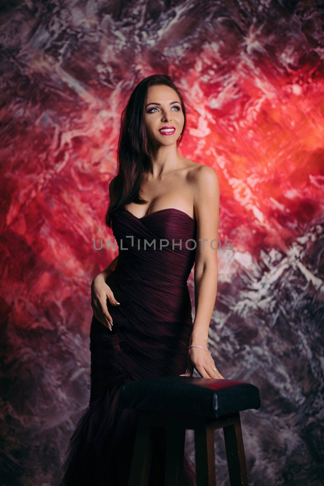 Portrait of magnificent sexy woman in evening dress posing over dark red background