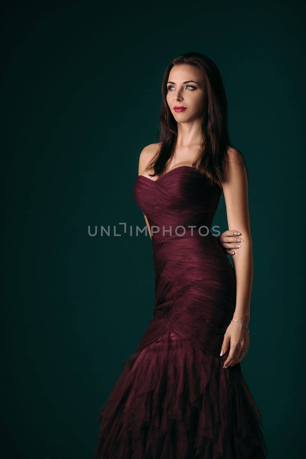 Portrait of magnificent sexy woman in evening dress posing over dark green background
