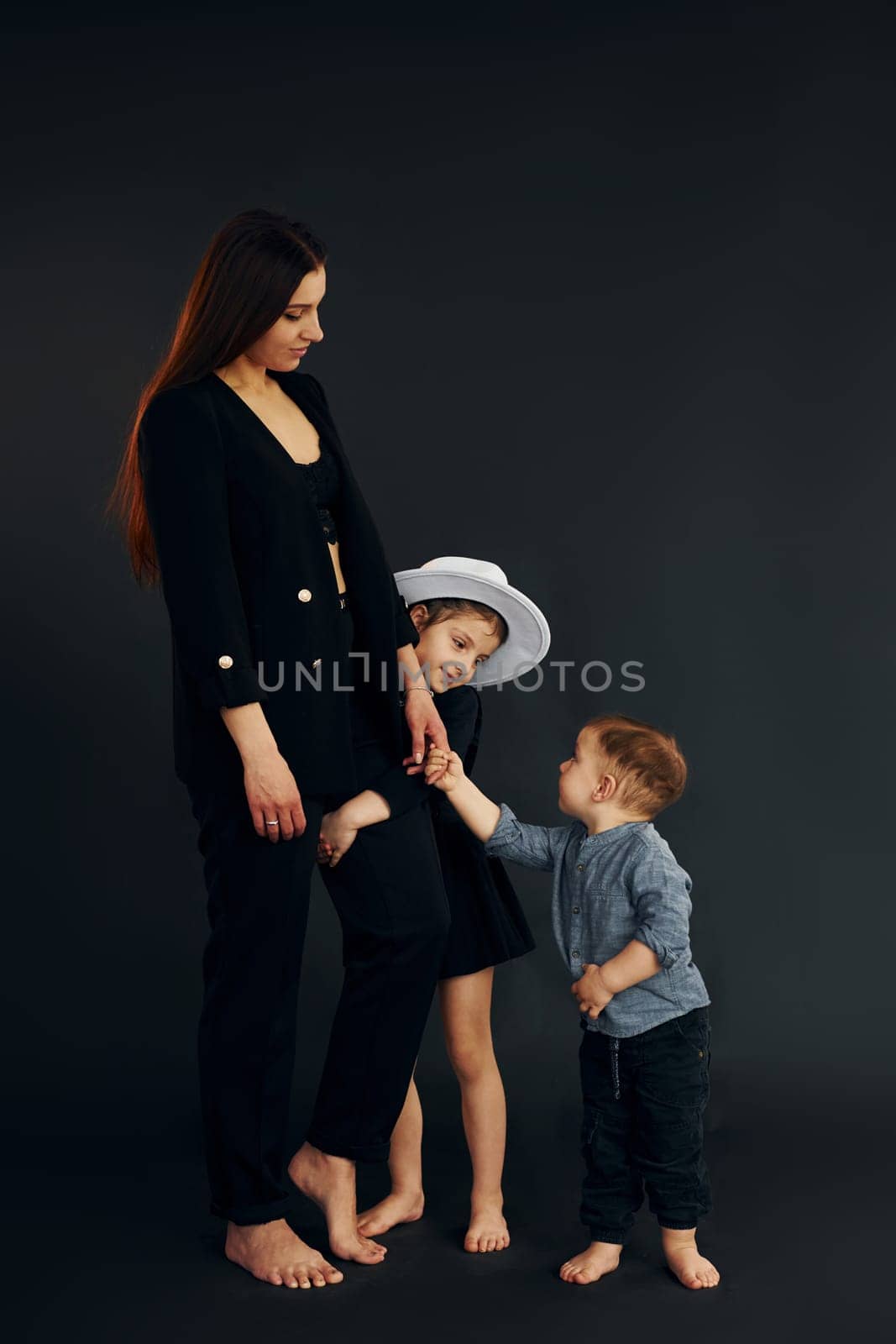Woman in black stylish clothes is with her little son and daughter in the studio.
