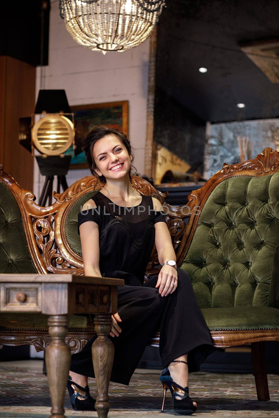 elegant smiling brunette woman with hairstyle in black clothes sits on a sofa
