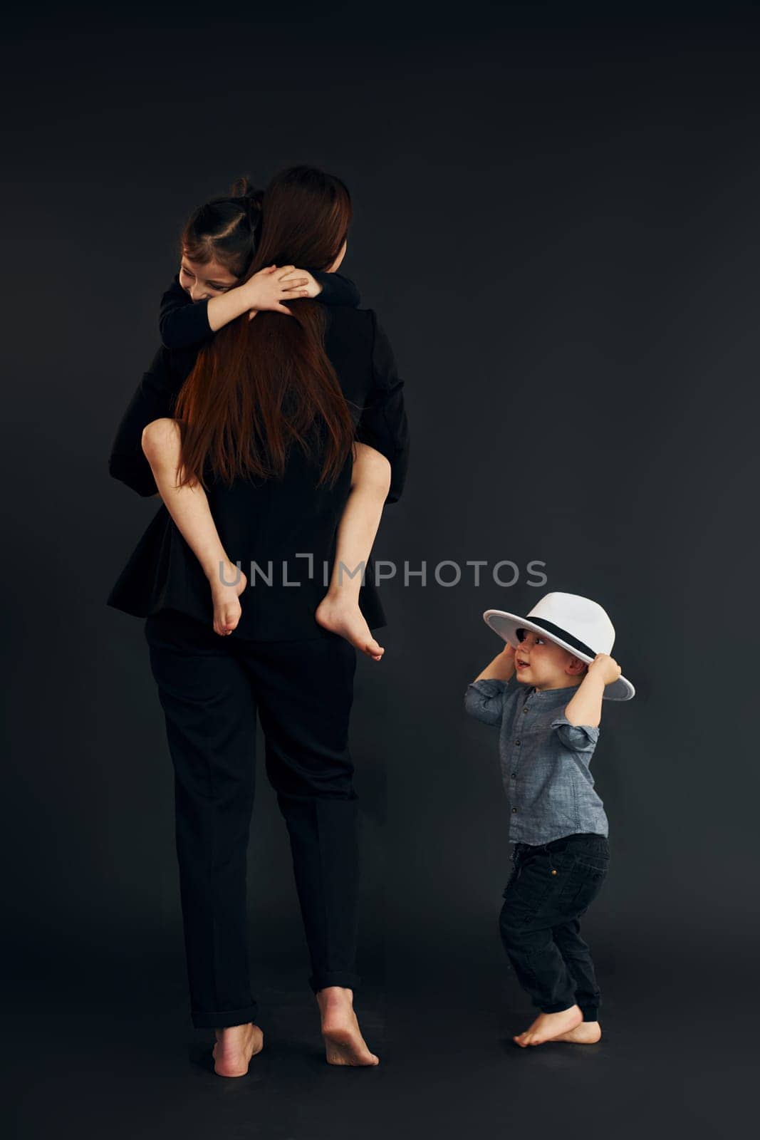 Woman in black stylish clothes is with her little son and daughter in the studio.