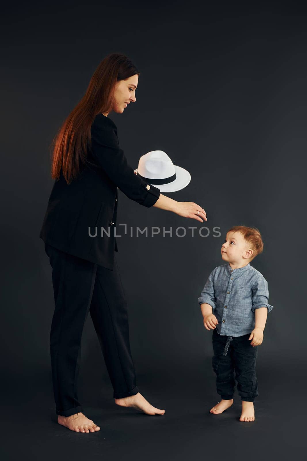 Mother in stylish black clothes is with her little son in the studio.