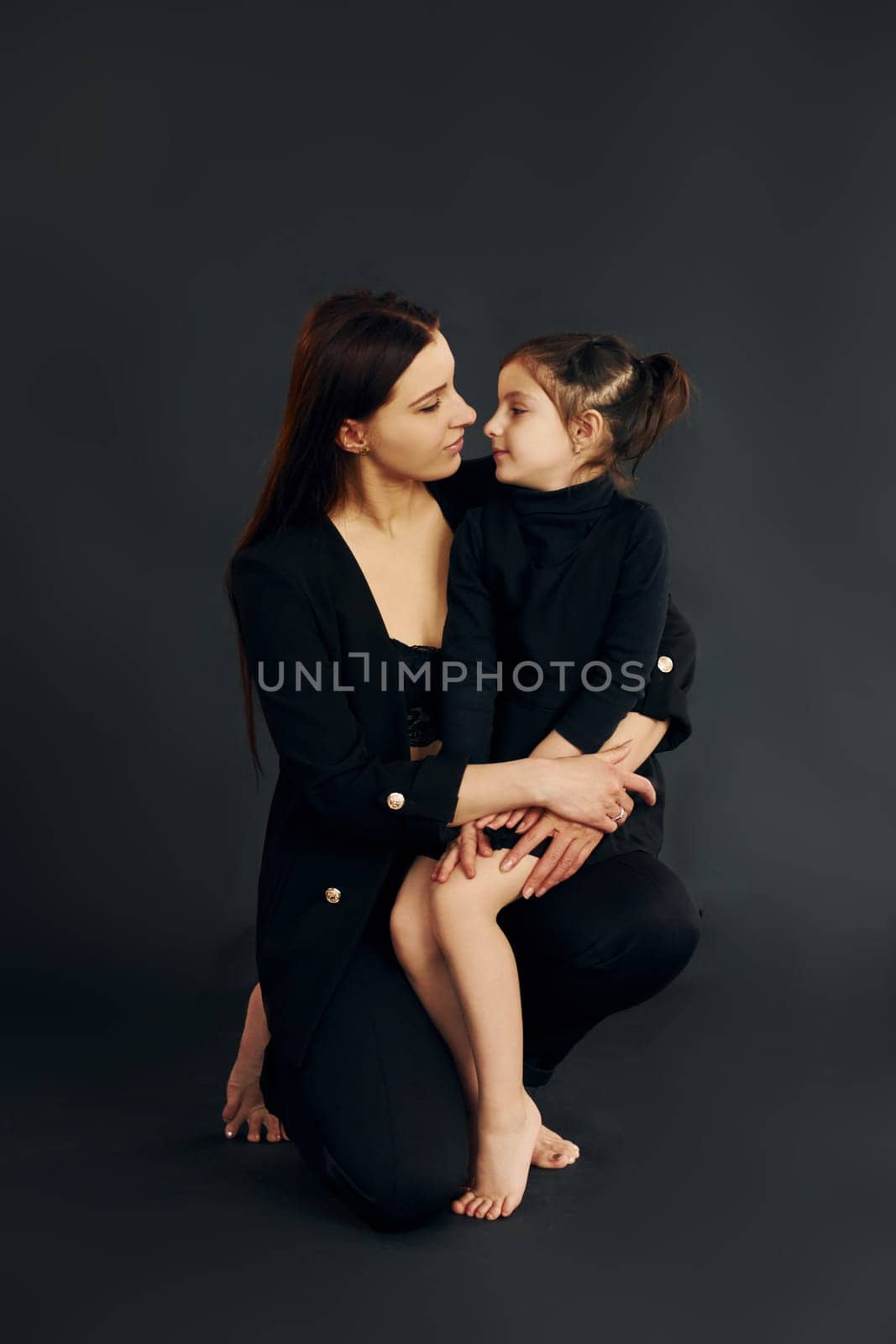 Mother and daughter is together in the studio against black background by Standret