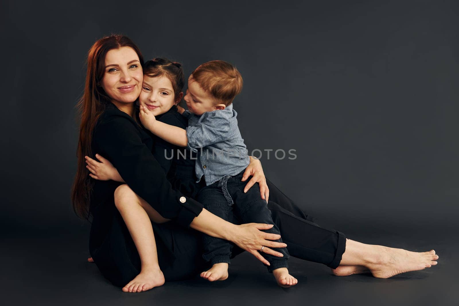 Woman in black stylish clothes is with her little son and daughter in the studio.