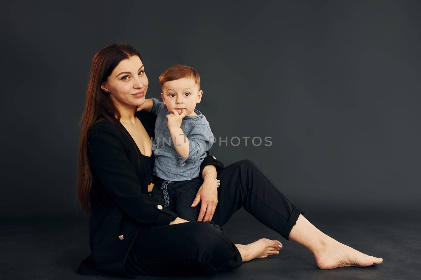 Sitting on the floor. Mother in stylish black clothes is with her little son in the studio by Standret