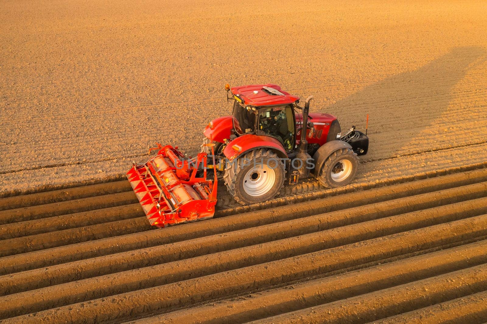 PRAGUE , CZECH REPUBLIC - MARCH 18 2022: Heavy tractor prepares soil making beds for planting in rural field. Agricultural machine operates at sunset in countryside aerial view