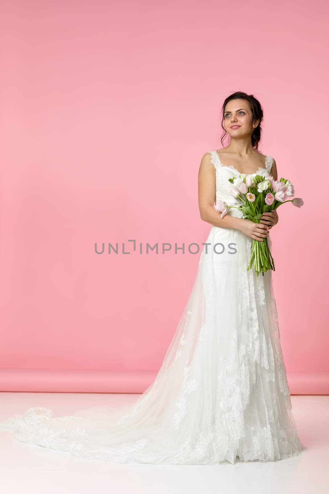 beautiful bride with wedding bouquet of pink tulips on pink background