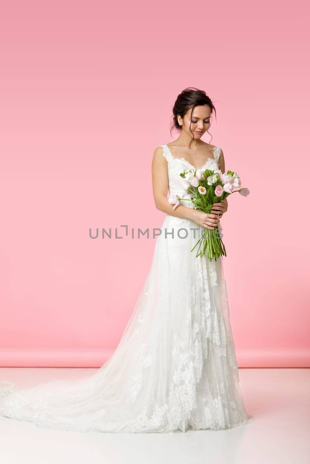 beautiful bride with wedding bouquet of pink tulips on pink background