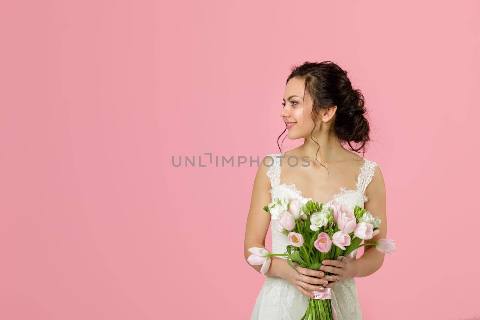 beautiful bride with wedding bouquet of pink tulips on pink background