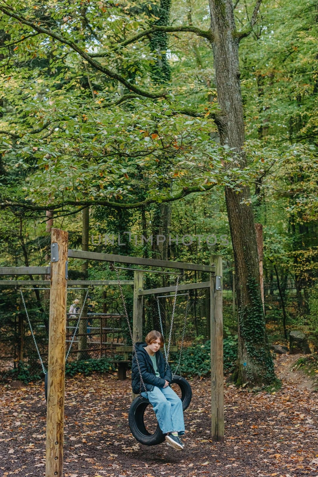 A teenage girl sitting on a swing on the park. Pensive sad child. Thoughtful Sad Teenager Girl Sitting On Playground Roundabout. teenage girl sad on the swing in the park. by Andrii_Ko