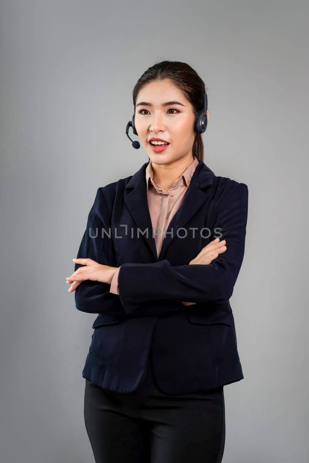 Attractive asian female call center operator with happy smile face advertises job opportunity on empty space, wearing a formal suit and headset on customizable isolated background. Enthusiastic