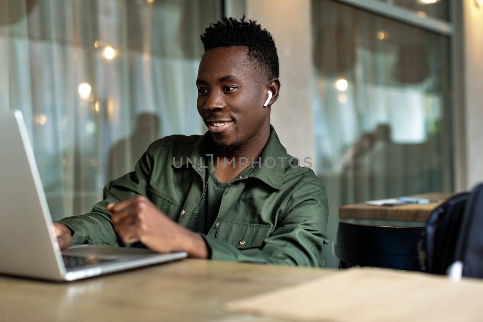 Cheerful young african american man in headphones using computer in cafe