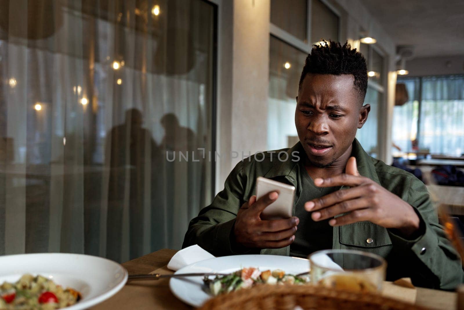 young disappointed surprised african american man messaging online, checking social networks in cafe. copy space