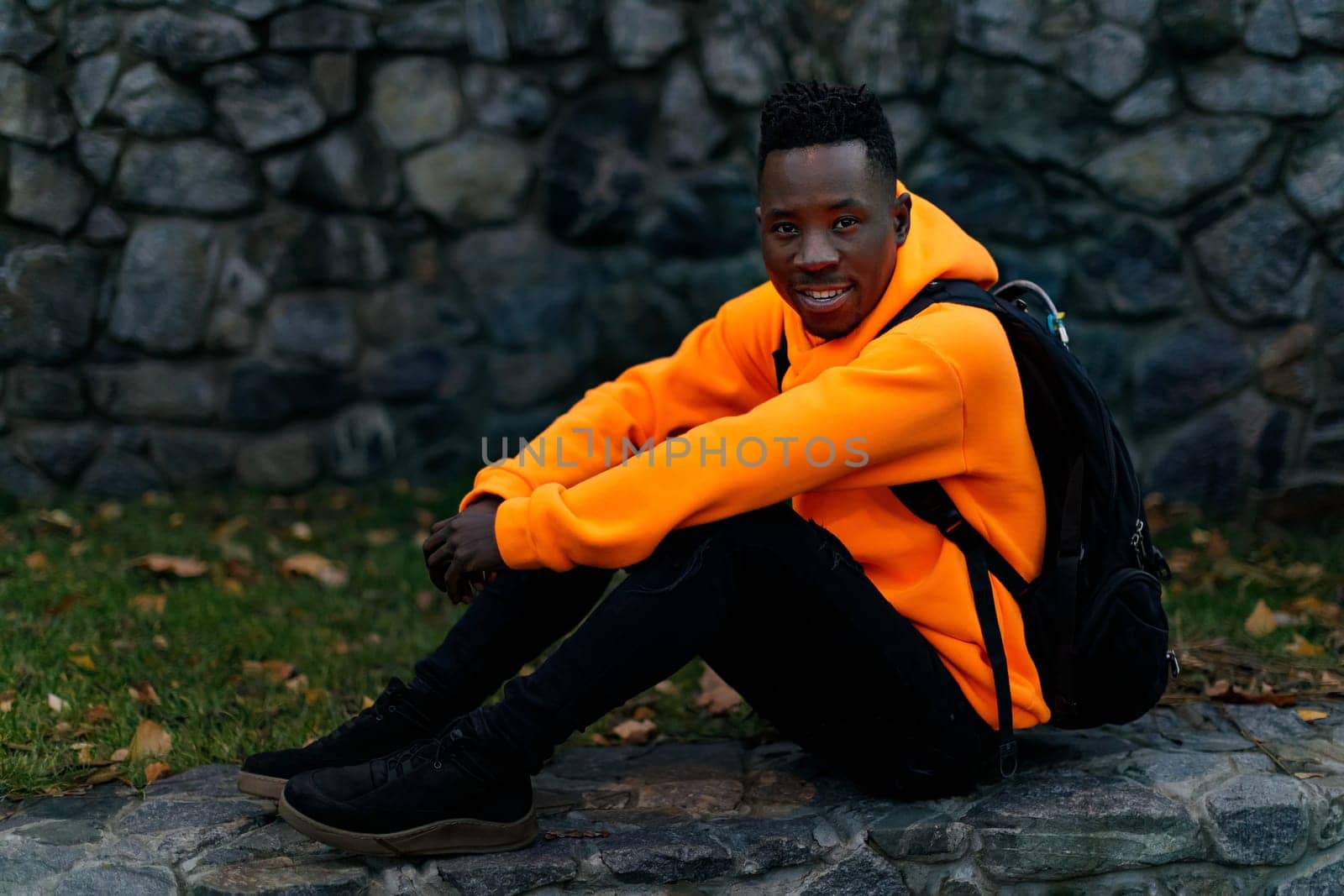 african-american man in stylish orange hoodie sweatshirt sitting outdoor