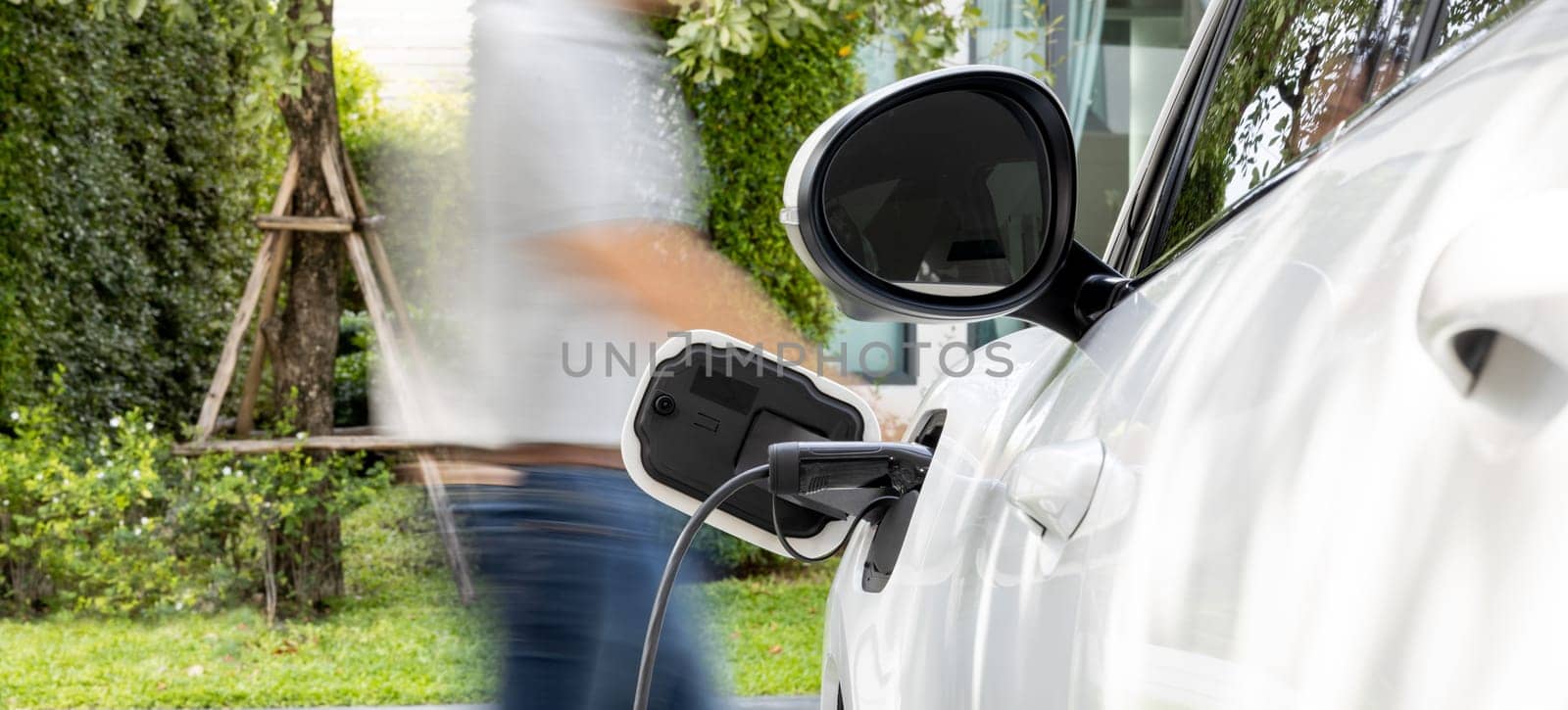 Focus recharging electric vehicle outdoor from charging station with motion blur background of man walking. Concept ideal for new progressive technology of green and renewable energy for electric car.