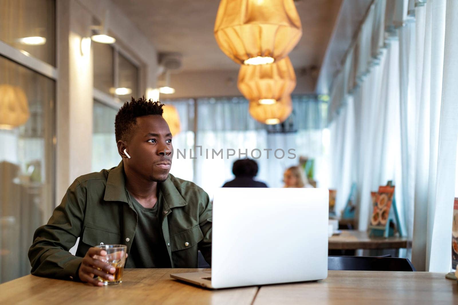 Cheerful young african american man in headphones using computer in cafe