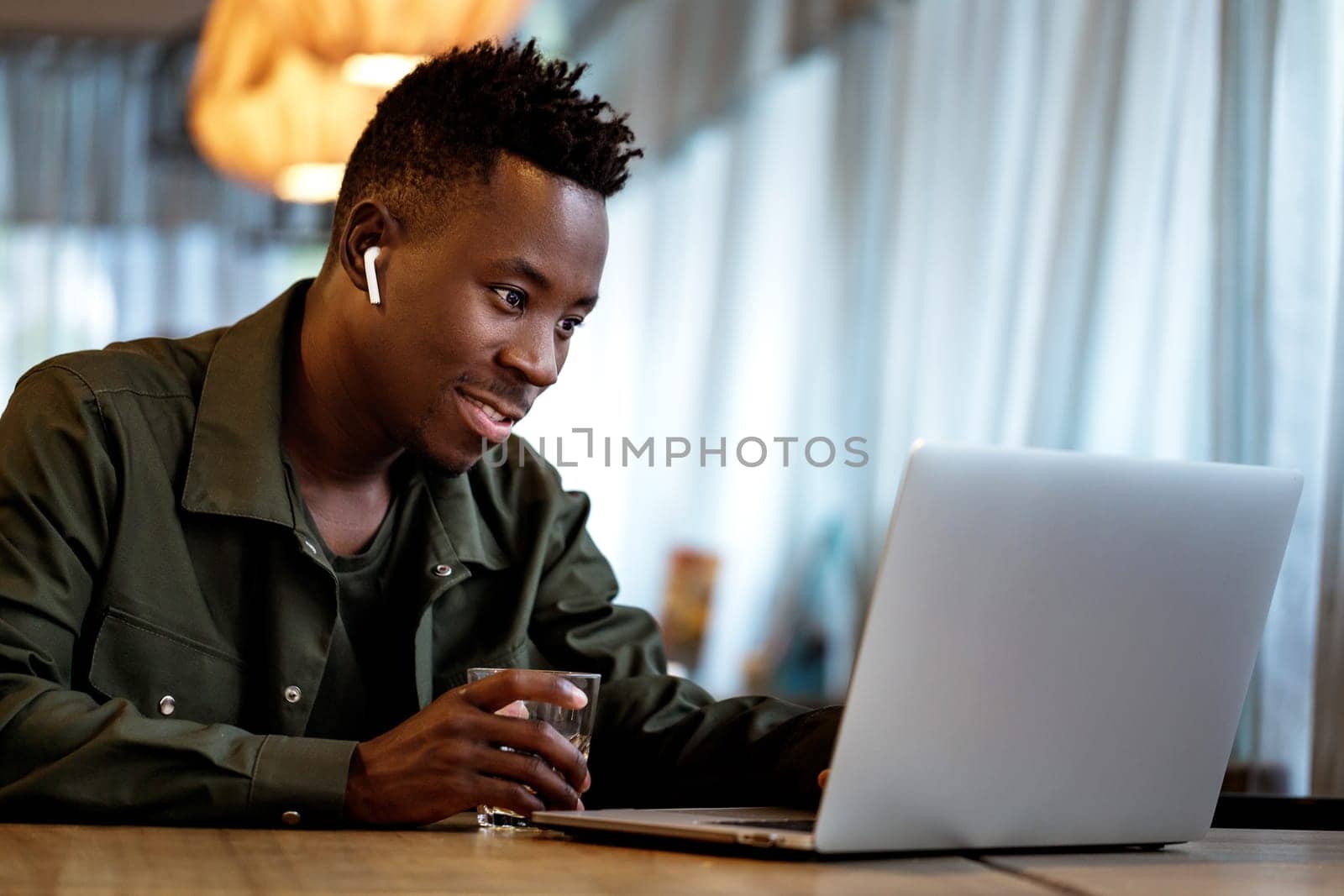Cheerful african american man in headphones using computer in cafe. young smiling businessman working on laptop. space for text